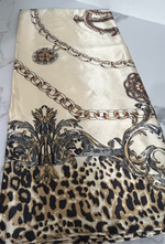 A folded silk scarf featuring a mixed print design with a leopard print bottom section, a gold chain motif, and ornate baroque scrollwork on a cream background.